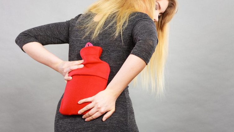 Tipps gegen Rückenschmerzen - Soforthilfe bei akuten Rückenschmerzen / Frau mit Wärmeflasche am Rücken bei Freizeit, Haus & Garten
